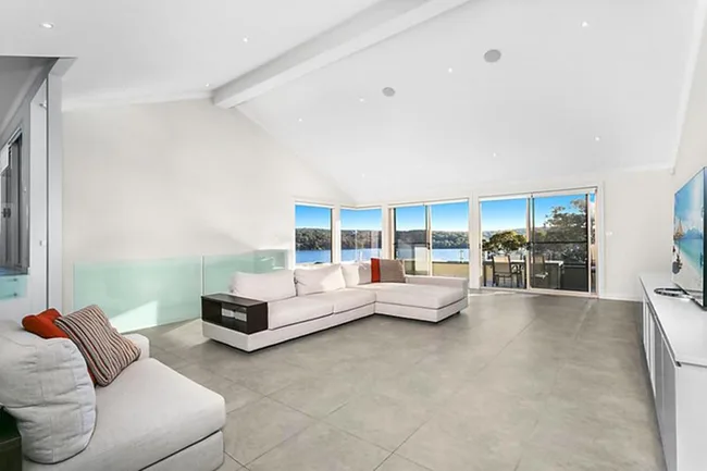 Spacious living room with beige sectional sofa, large windows showcasing a scenic view, modern decor, and a flat-screen TV.
