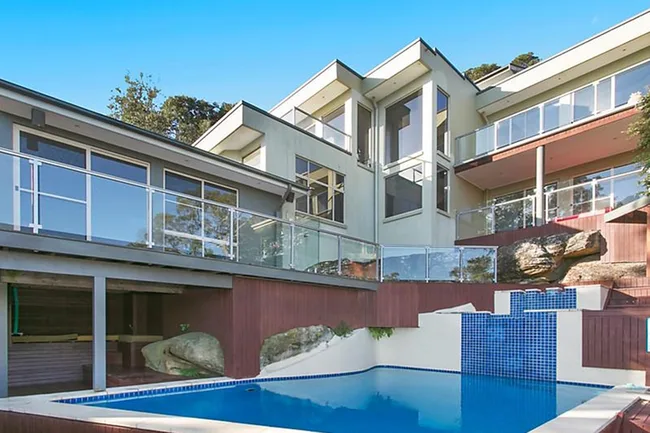 Modern multi-level house with large windows and glass railings, featuring a pool with blue tile accents.