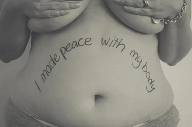 A woman's torso with the phrase "I made peace with my body" written on her stomach.