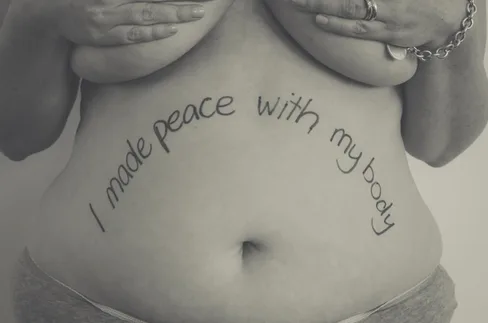 A woman's torso with the phrase "I made peace with my body" written on her stomach.