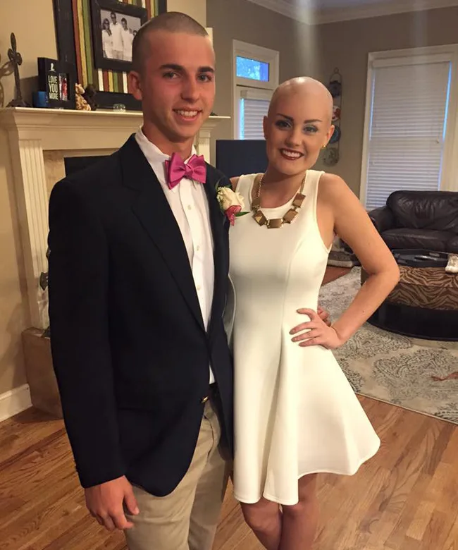 Man and woman dressed formally, smiling in a living room. The woman is wearing a white dress and the man a dark suit.