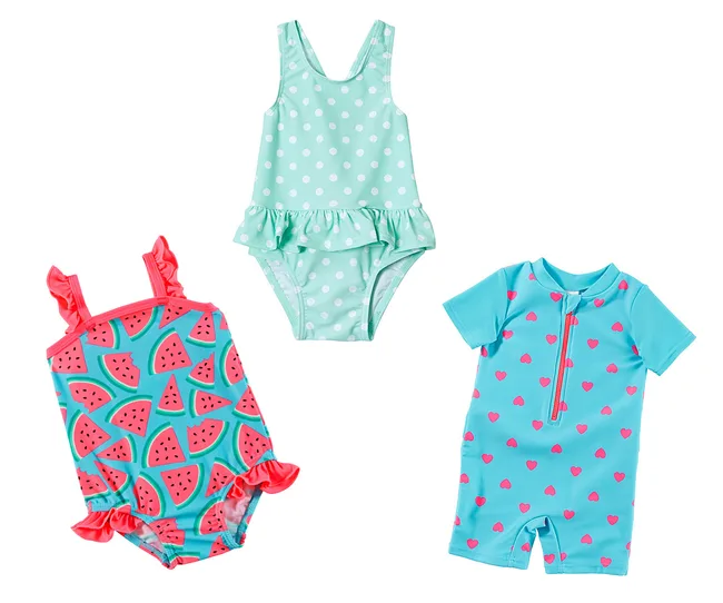 Three children's swimsuits: one with watermelon print, one polka-dotted with ruffles, and a teal with pink hearts.