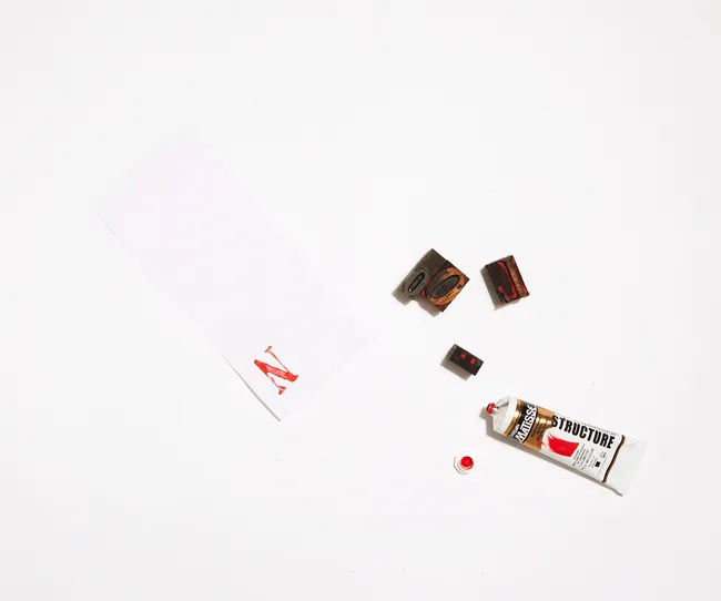 Red paint tube, stamps, and paper with airplane print on white background.