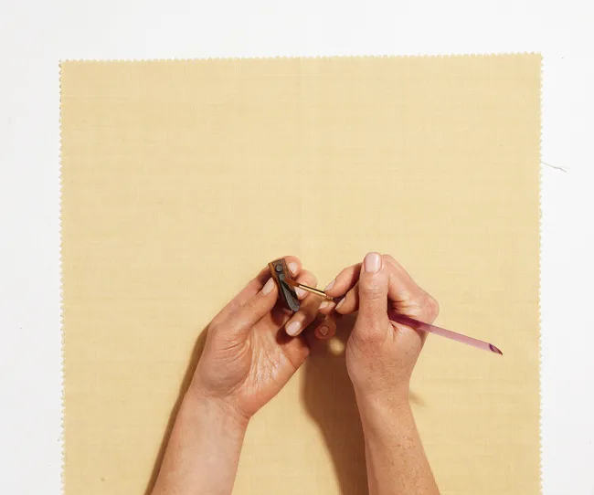 Hands holding a small tool, crafting on a textured fabric background.