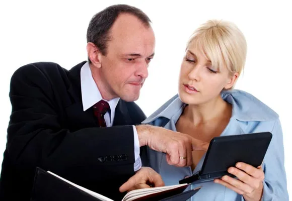 Man and woman discussing content on a tablet, with the man pointing and the woman observing intently.