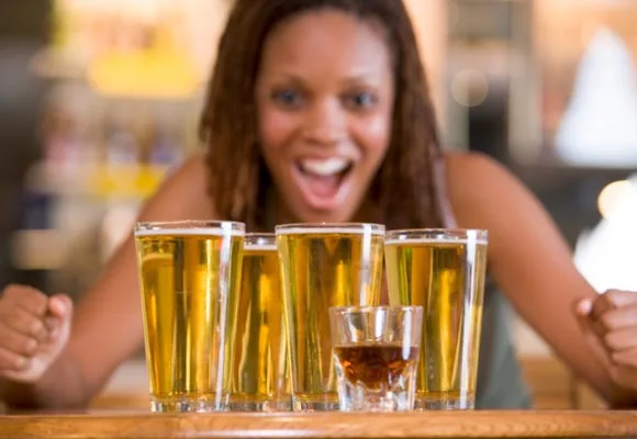 A person excitedly looks at several glasses of beer and one shot glass on a bar counter.
