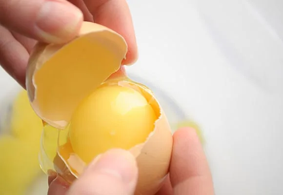 Hands holding a split egg revealing the yolk inside the shell.