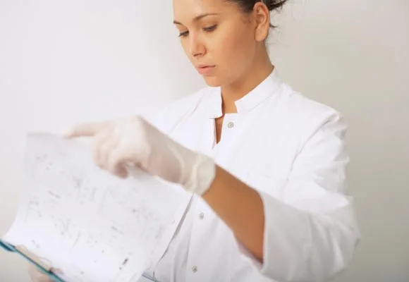 Female scientist in a lab coat and gloves examines data on a sheet of paper.