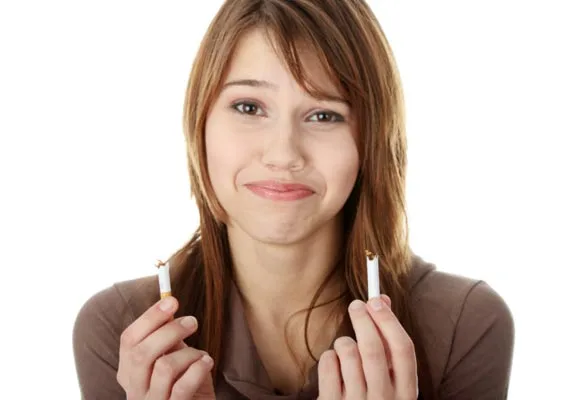 Young woman smiling while holding a broken cigarette, symbolizing quitting smoking.