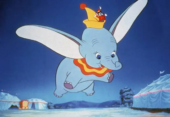 Dumbo, the flying elephant, soars with Timothy the mouse on his hat against a circus backdrop in a nighttime scene.