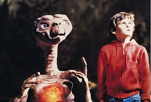 Boy in red hoodie looks up beside E.T., an alien with a glowing heart, from the movie "E.T. the Extra-Terrestrial."