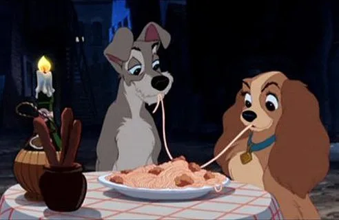 Two animated dogs, one gray and one brown, share a spaghetti dinner by candlelight at an outdoor table.
