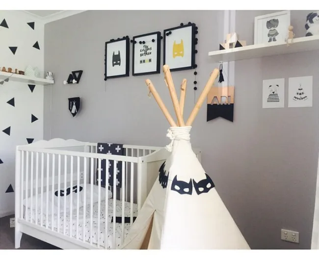 Nursery with a crib, teepee with superhero theme, and wall art including Batman masks and triangles.