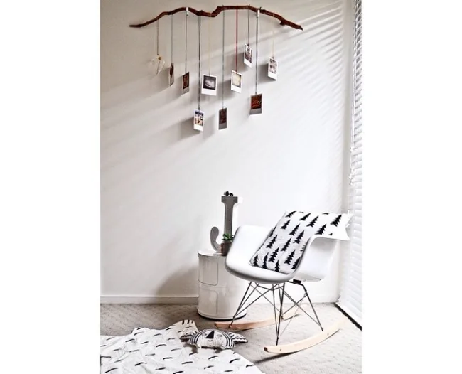 Minimalist room with a white rocking chair, hanging branch photo display, blanket, and soft lighting.