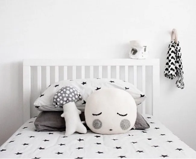 Cozy white bed with star-patterned bedding, cute face and mushroom pillows, and a polka dot scarf hanging nearby.