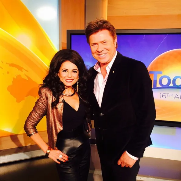 Two people posing and smiling in a TV studio, with a "Today" show screen in the background.