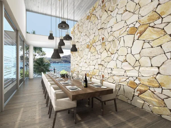 Contemporary dining room with stone accent wall, long wooden table set for dining, overlooking a scenic tropical view.