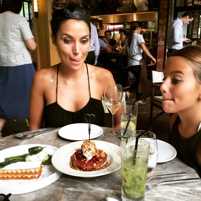 Two people making funny faces at a restaurant table with desserts and drinks.