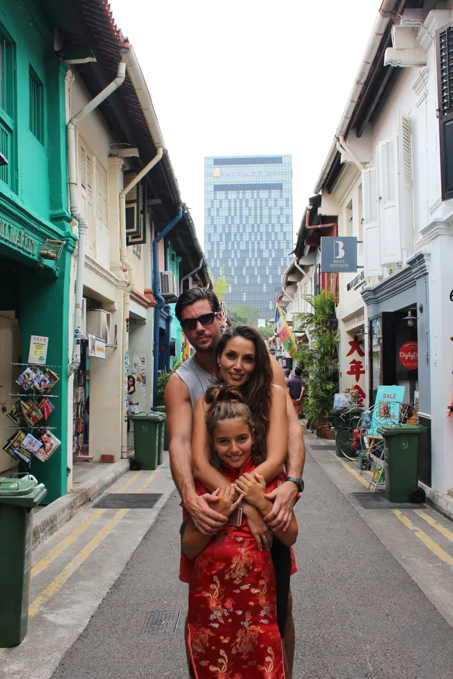 Family posing in a narrow street lined with colorful buildings, with a modern skyscraper in the background.
