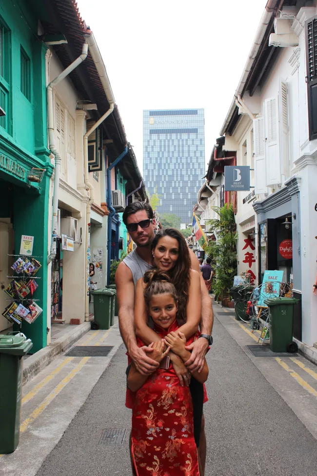 Family posing in a narrow street lined with colorful buildings, with a modern skyscraper in the background.