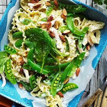 A plate of pasta with creamy sauce, sugar snap peas, spinach, and almonds on a blue speckled dish.