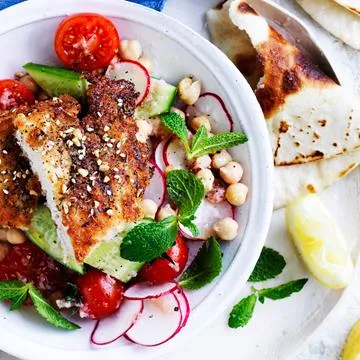 Grilled fish with avocado, cherry tomatoes, radishes, chickpeas, and mint leaves served in a white bowl.