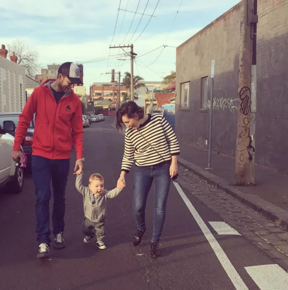 Man and woman walk with toddler holding hands on a street. Urban background with graffiti.