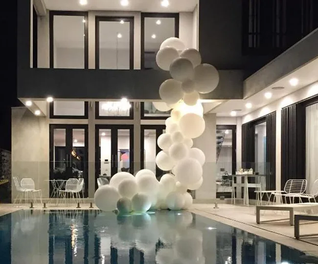 Modern house with glass walls, white balloon cluster, and pool at night.