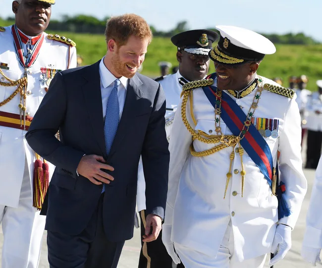 Two men smiling and walking; one in a suit, the other in a military uniform with medals and a sash.