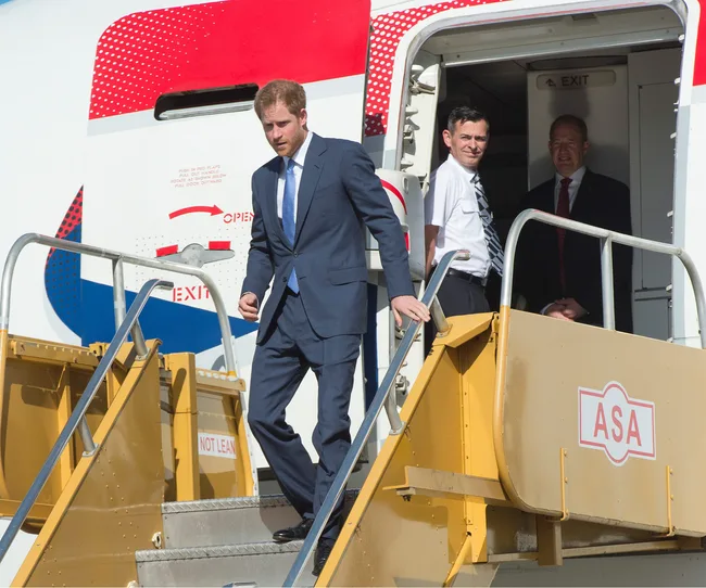 Man in suit descends airplane stairs, followed by two men in aviation attire at the door.