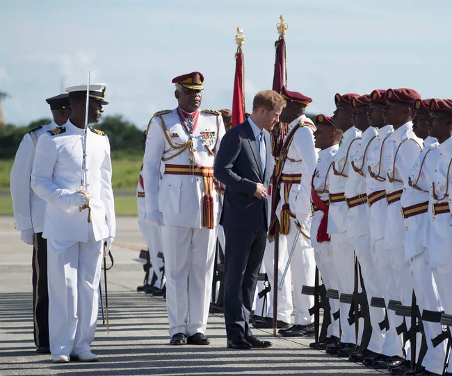 A man in a suit inspects a line of soldiers in white uniforms with red berets and medals during an outdoor ceremony.