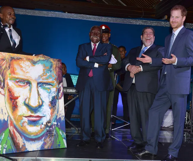 Group of men in suits stand on stage smiling beside a colorful portrait painting.