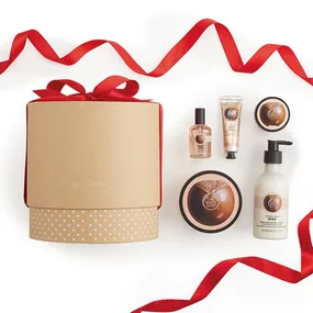 Gift box with red ribbon, surrounded by various Body Shop products like creams and lotions, on a white background.