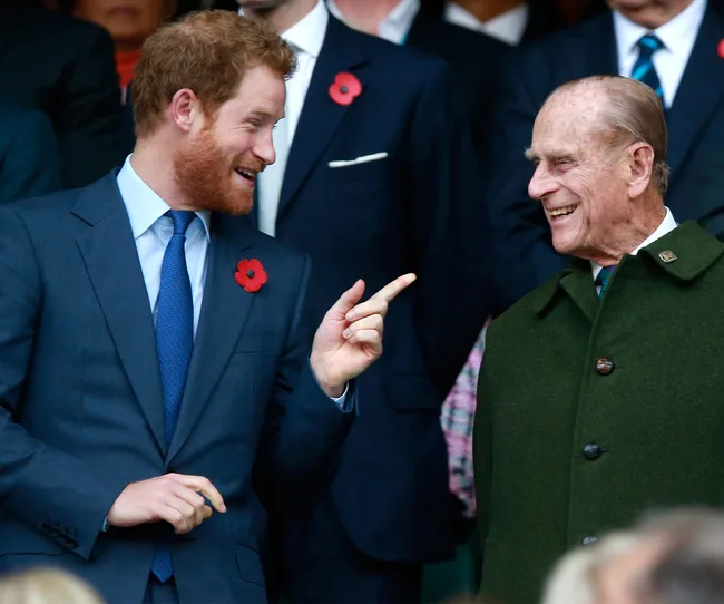 Two men in suits, smiling and interacting, wearing poppy pins at a formal event.