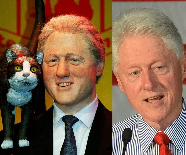 A wax figure and a real person, both older men with white hair, the figure with a cat and wearing a suit; the real man speaks.