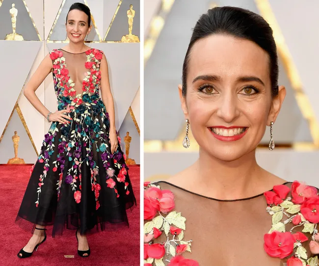 Woman in a floral embroidered gown at a red carpet event, smiling with hair up and wearing drop earrings.