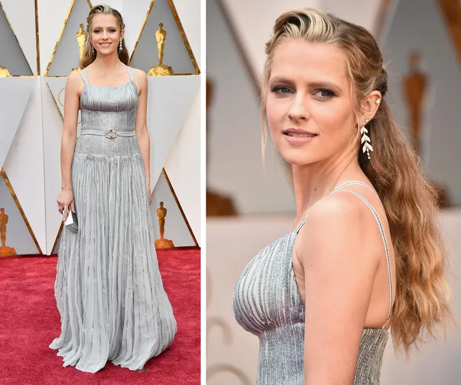 Elegant woman in a silver gown on the red carpet at a formal event, with wavy hair and statement earrings.