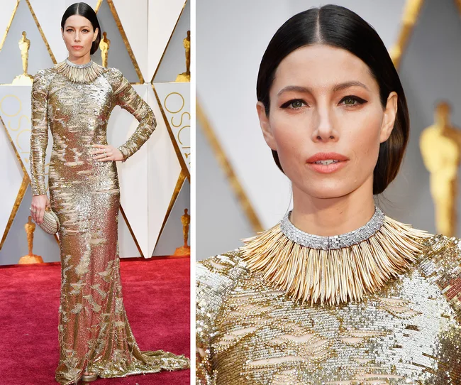 Golden sequined dress with metallic collar detail on the Oscars red carpet. Woman poses with sleek hairstyle and clutch.