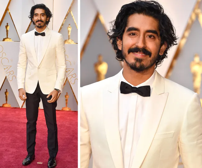A person in a white tuxedo with a black bowtie smiles on the Oscar red carpet.