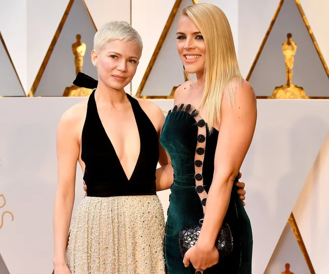 Two women posing on a red carpet, one with a pixie cut and another with long hair, both in elegant dresses.