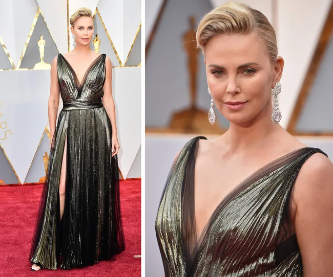 Woman in a metallic gold gown with a deep V-neck and a slit, standing on a red carpet, wearing drop earrings.