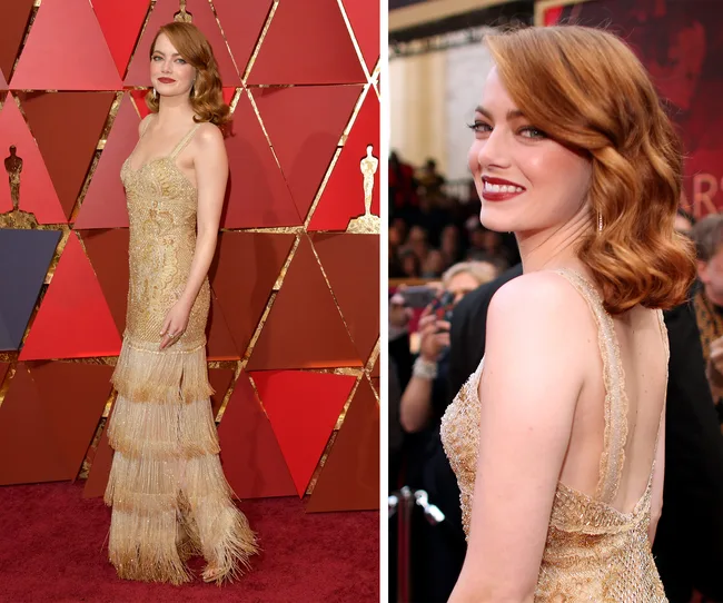 Woman in a gold gown on the red carpet, posing in front of geometric red and brown backdrop.