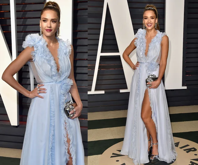 A woman in a blue ruffled gown with a high slit, holding a silver clutch, posing at a formal event.