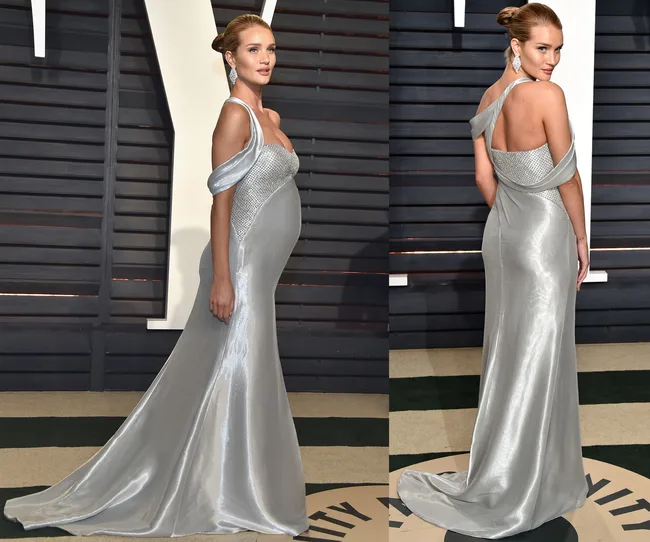 Elegant woman in a silver gown poses at a formal event, showcasing the dress&rsquo;s design from the side and back.
