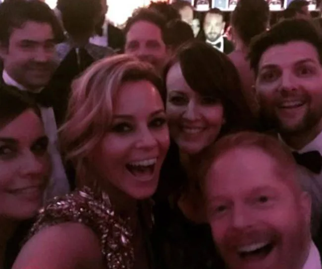 Group of people in formal attire smiling and taking a selfie at an event.