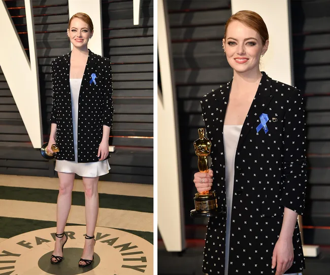 Person in a patterned blazer with a blue ribbon, holding an Oscar statue at an event.