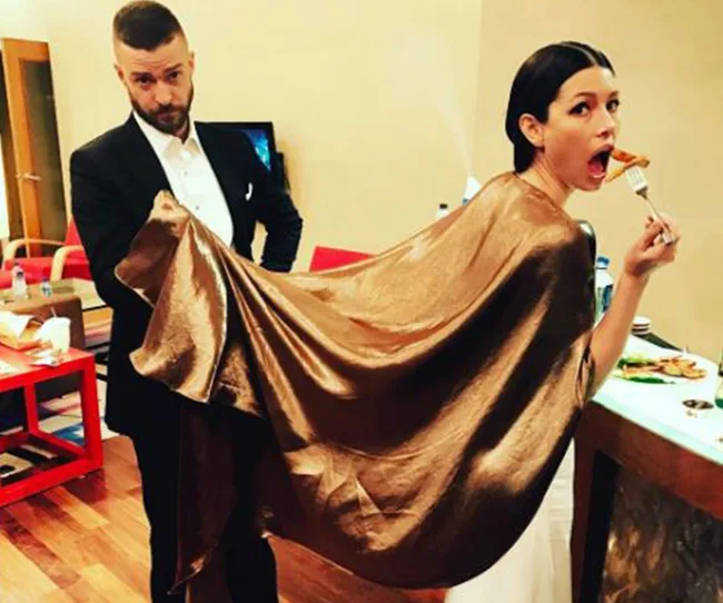 Man holding cape of woman eating pizza in a glamorous room.