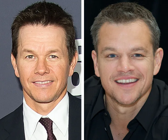 Two men with short dark hair smiling; one wears a suit and tie, the other a black shirt.