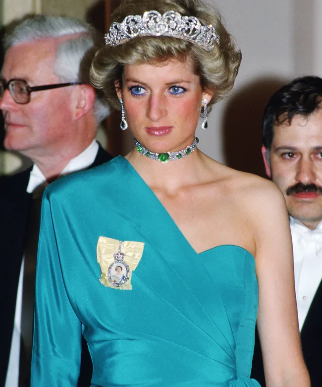 Princess Diana wearing a tiara and emerald jewelry, in a teal dress at a formal event.