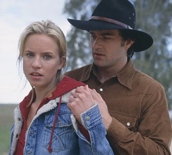 Man in a cowboy hat holding a woman in a denim jacket outdoors.